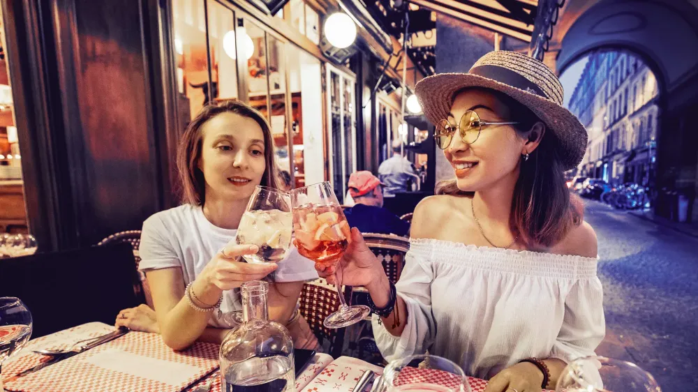 Two mixed race girls friends clinking glasses while enjoying an celebrating moment in cafe at evening time